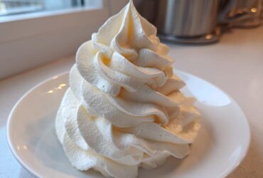 A tall, perfectly piped swirl of creamy white vanilla buttercream frosting sitting on a small white saucer.