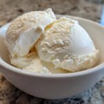 Close-up of three scoops of creamy, vanilla-colored protein ice cream served in a small white bowl.