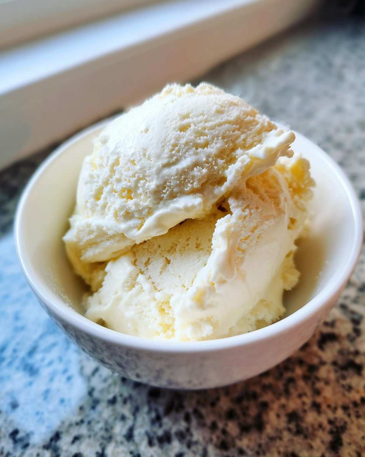 Close-up of two scoops of creamy vanilla protein ice cream served in a small white bowl.