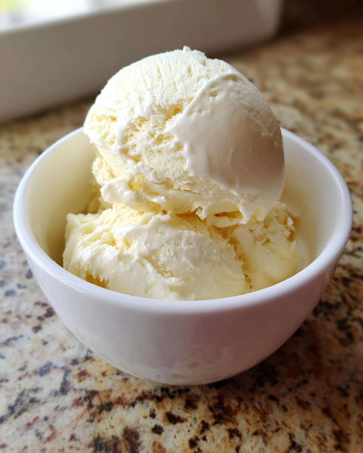 Two scoops of creamy, pale yellow protein ice cream melting slightly in a small white bowl.
