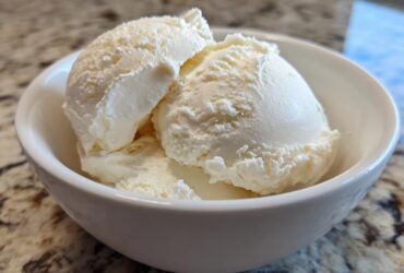Close-up of three scoops of creamy, vanilla-colored protein ice cream served in a small white bowl.
