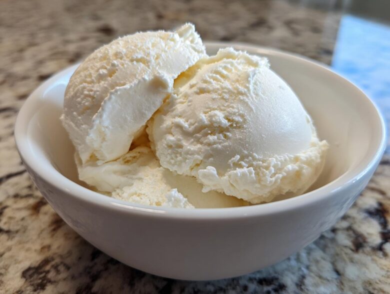 Close-up of three scoops of creamy, vanilla-colored protein ice cream served in a small white bowl.