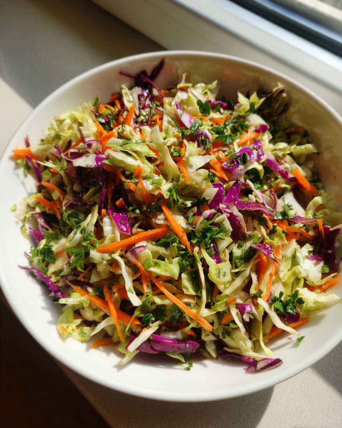 Close-up of a vibrant cabbage salad featuring shredded green cabbage, purple cabbage, carrots, and parsley.