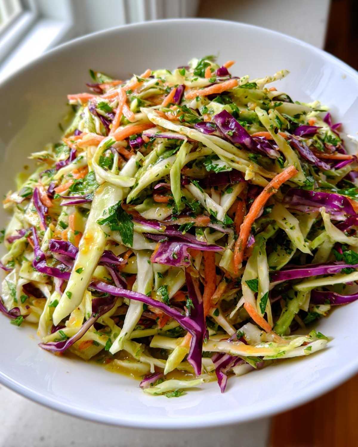 Close-up of a vibrant cabbage salad featuring shredded green and red cabbage, carrots, and herbs in a white bowl.