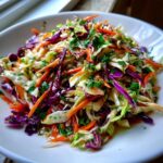 Close-up of a vibrant, freshly dressed cabbage salad featuring shredded green and red cabbage, carrots, and parsley.