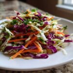 A vibrant mound of freshly prepared cabbage salad featuring shredded white and purple cabbage, carrots, and parsley garnish.