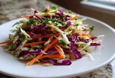 A vibrant mound of freshly prepared cabbage salad featuring shredded white and purple cabbage, carrots, and parsley garnish.