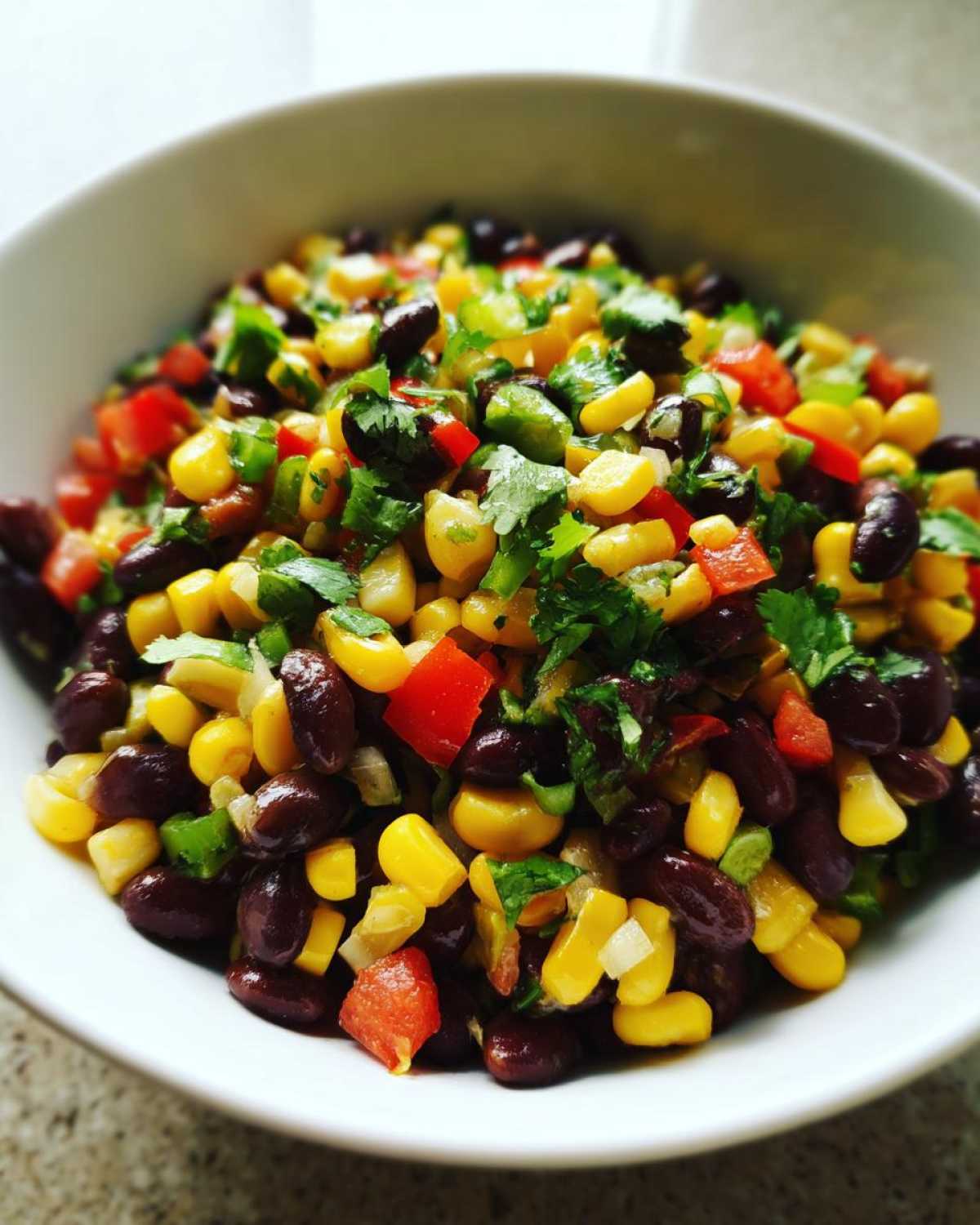 Close-up of vibrant cowboy caviar dip featuring black beans, corn, red peppers, and cilantro in a white bowl.