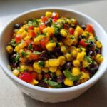 Close-up of colorful cowboy caviar dip featuring corn, black beans, red peppers, and cilantro in a white serving bowl.