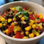Close-up of colorful cowboy caviar dip featuring black beans, corn, tomatoes, and cilantro in a white serving bowl.