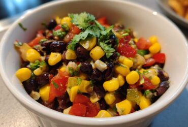 Close-up of colorful cowboy caviar dip featuring black beans, corn, tomatoes, and cilantro in a white serving bowl.
