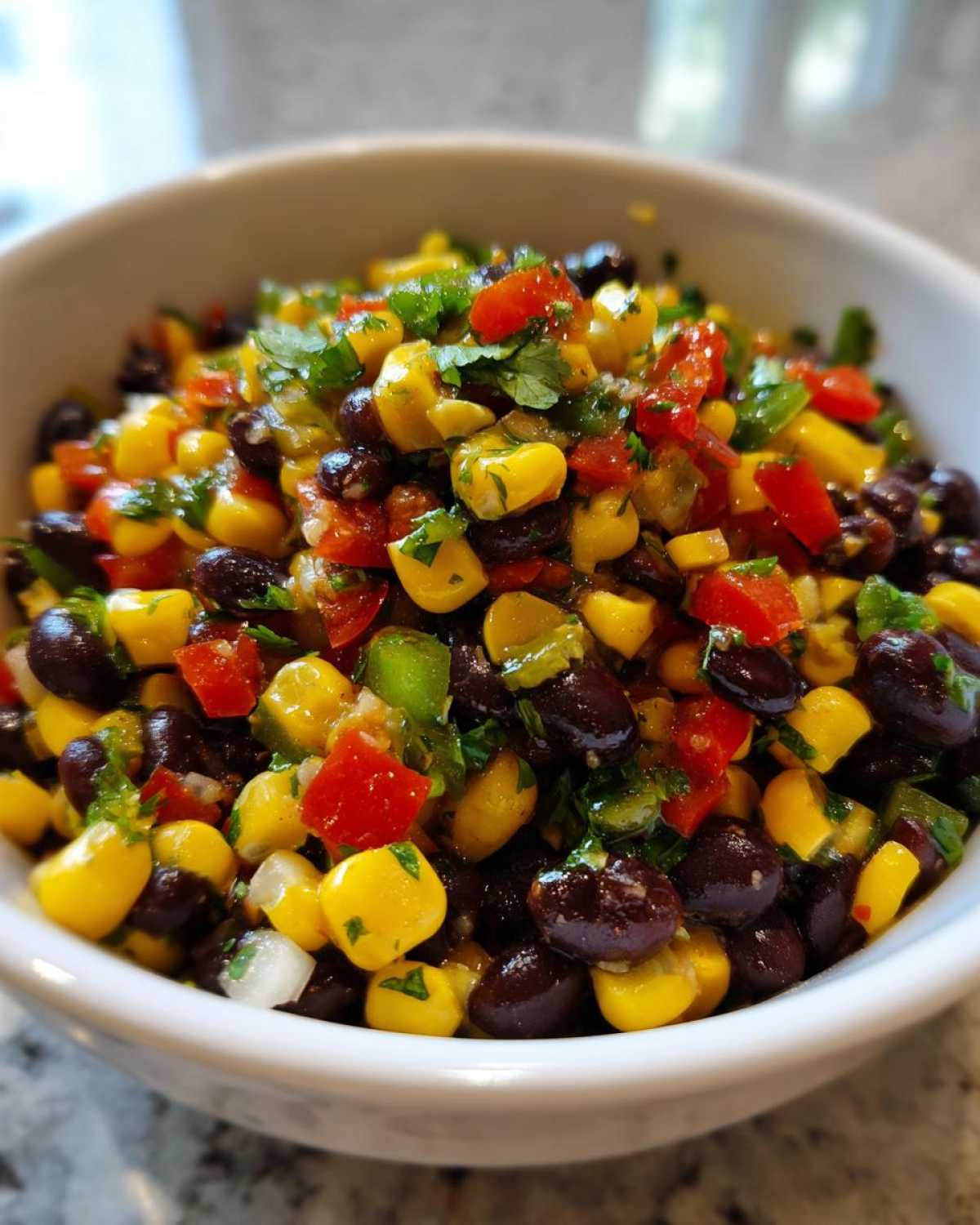 Close-up of colorful cowboy caviar dip featuring black beans, corn, red peppers, and cilantro in a white bowl.