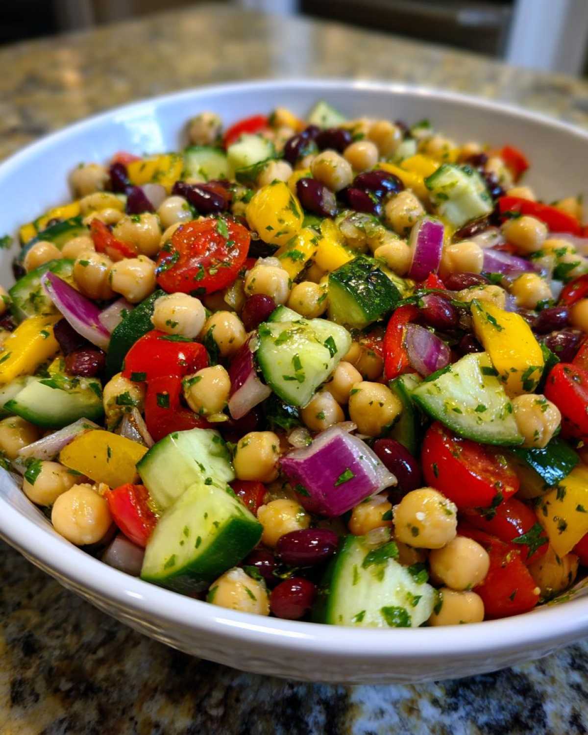 Close-up of a vibrant, colorful bean salad featuring chickpeas, kidney beans, cucumber, tomato, and red onion.