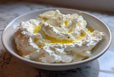 A close-up of creamy, fluffy whipped feta dip topped with golden olive oil in a white bowl.