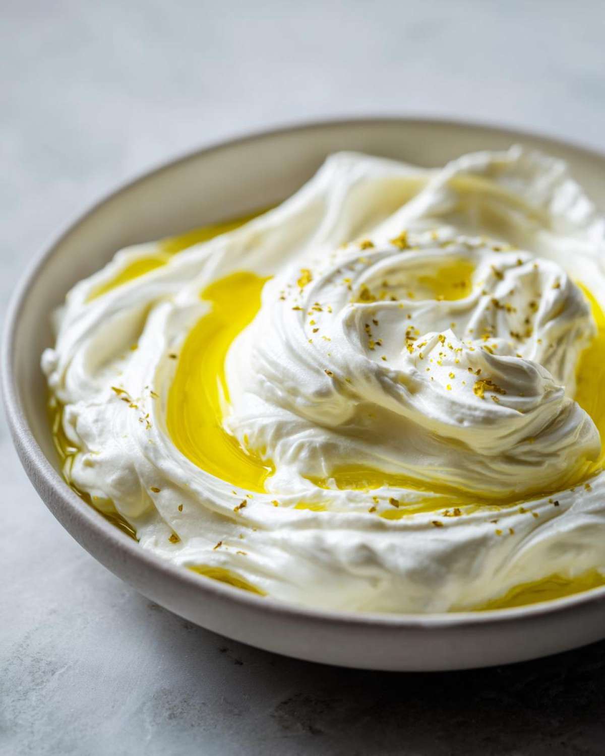 Close-up of a bowl of creamy whipped feta dip drizzled with bright yellow olive oil and sprinkled with herbs.