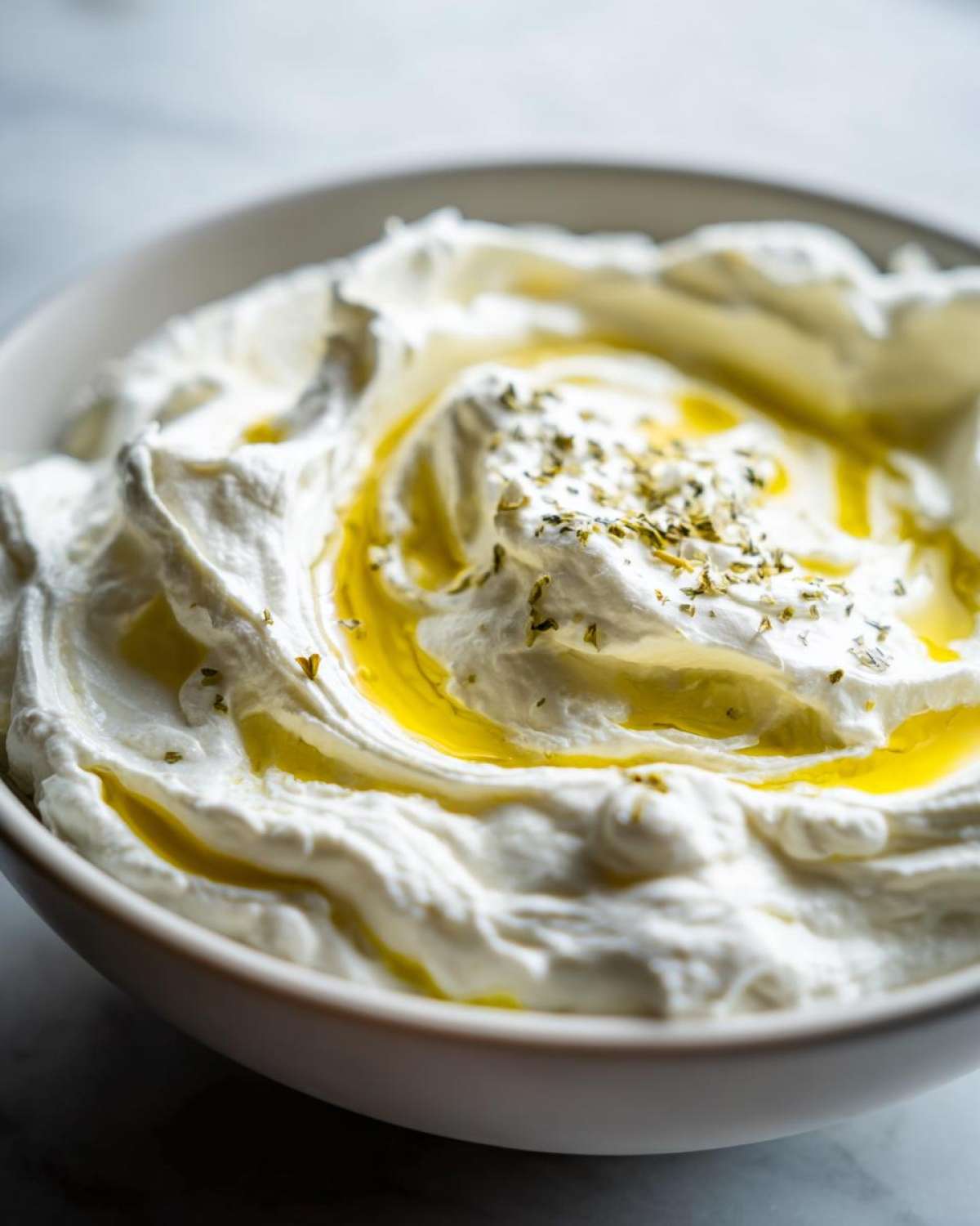 Close-up of a bowl of freshly made whipped feta dip, swirled with olive oil and sprinkled with herbs.