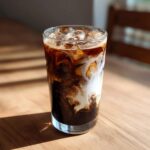 Close-up of a tall glass filled with an Iced Mocha showing rich dark coffee swirling beautifully with white milk over ice.