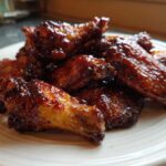 Close-up of glossy, saucy Air Fryer BBQ Chicken Wings piled high on a white plate.