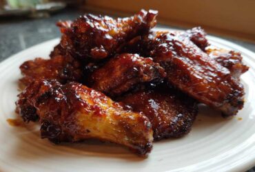 Close-up of glossy, saucy Air Fryer BBQ Chicken Wings piled high on a white plate.