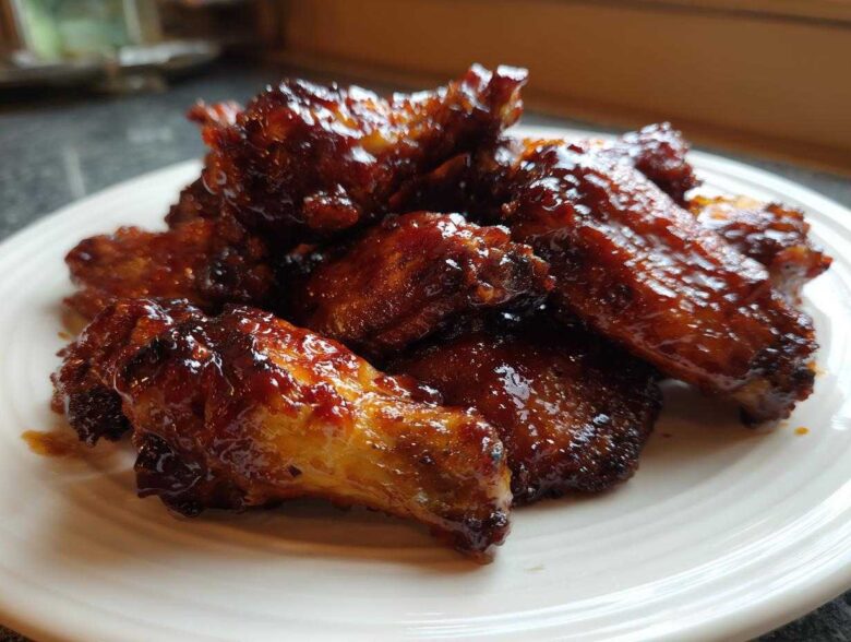 Close-up of glossy, saucy Air Fryer BBQ Chicken Wings piled high on a white plate.