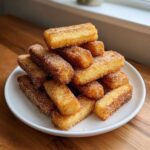 A tall pile of golden brown Air Fryer French Toast Sticks coated generously with cinnamon sugar on a white plate.