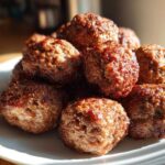 A pile of golden-brown, juicy Air Fryer Italian Meatballs stacked on a white plate, catching sunlight.