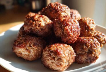 A pile of golden-brown, juicy Air Fryer Italian Meatballs stacked on a white plate, catching sunlight.