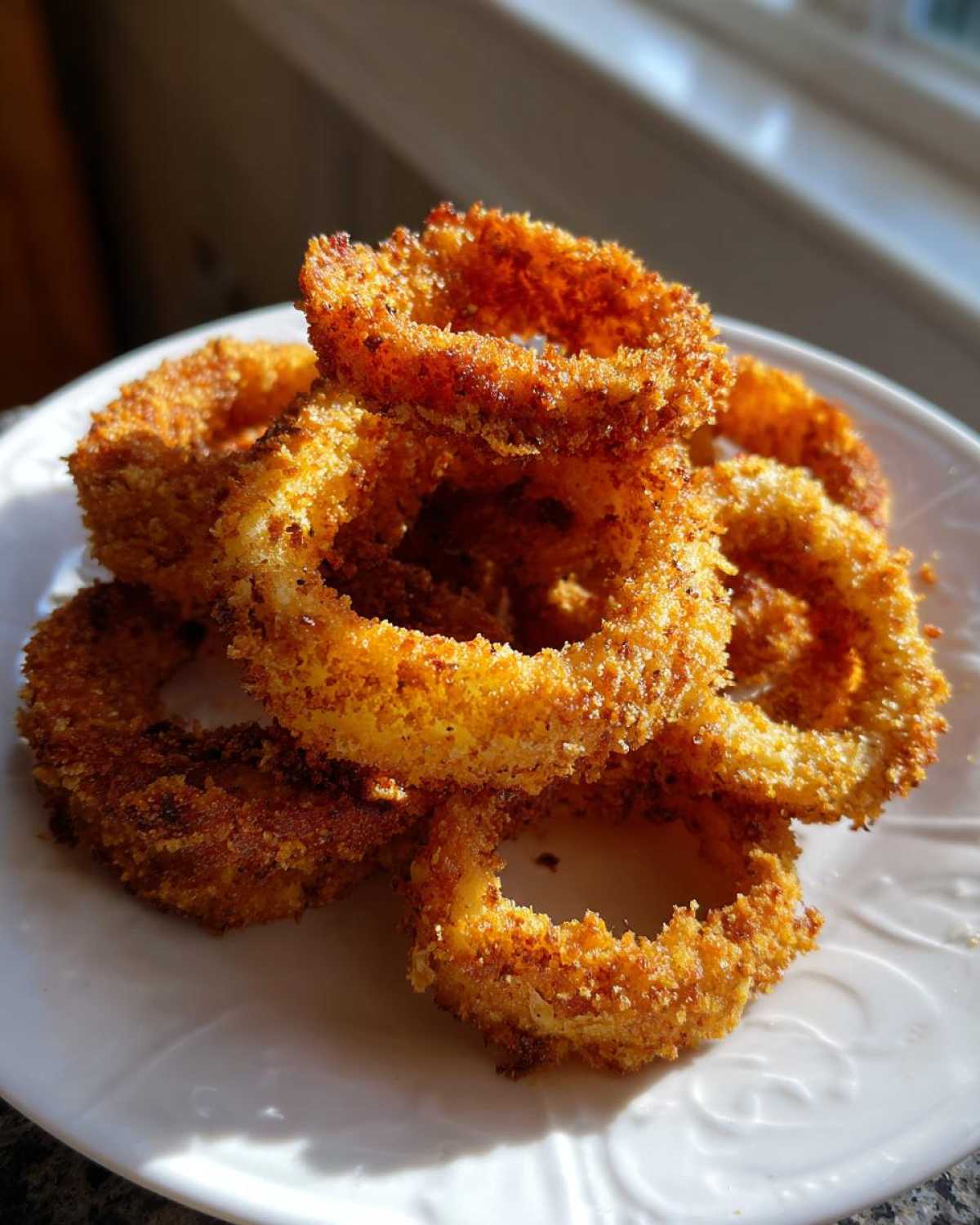 A close-up of several golden brown, crispy Air Fryer Onion Rings stacked on a white plate.