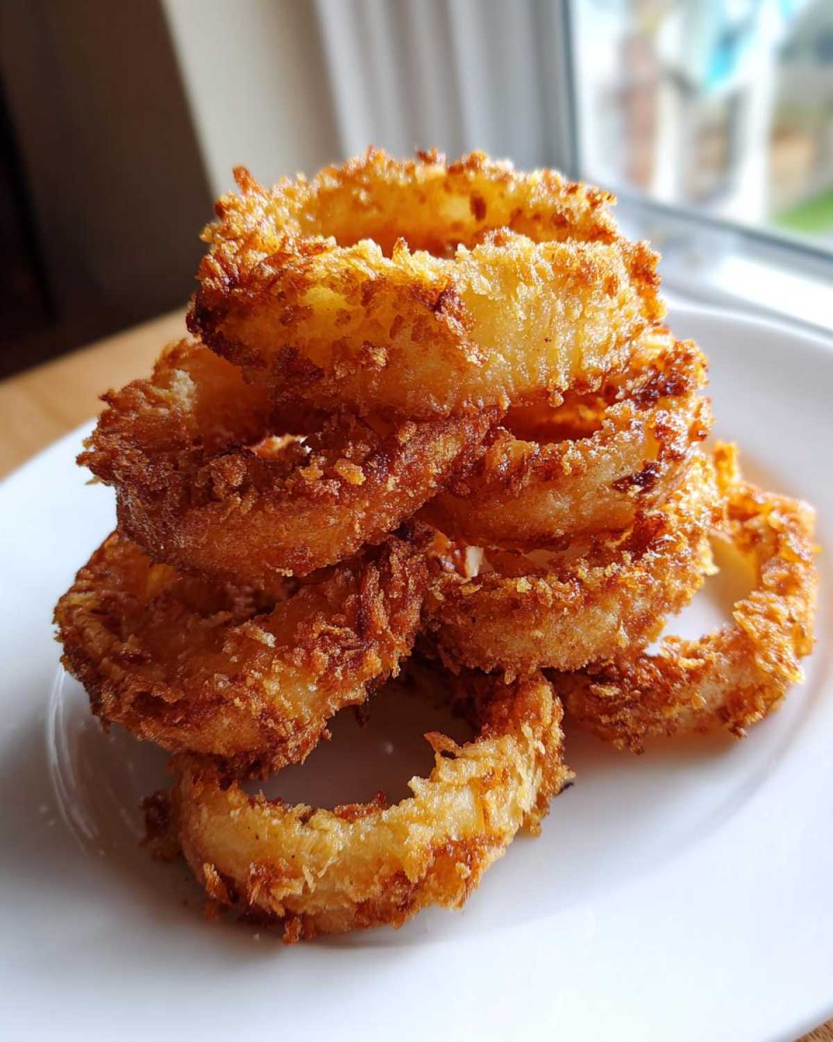 A tall stack of golden brown, crispy Air Fryer Onion Rings piled high on a white plate.