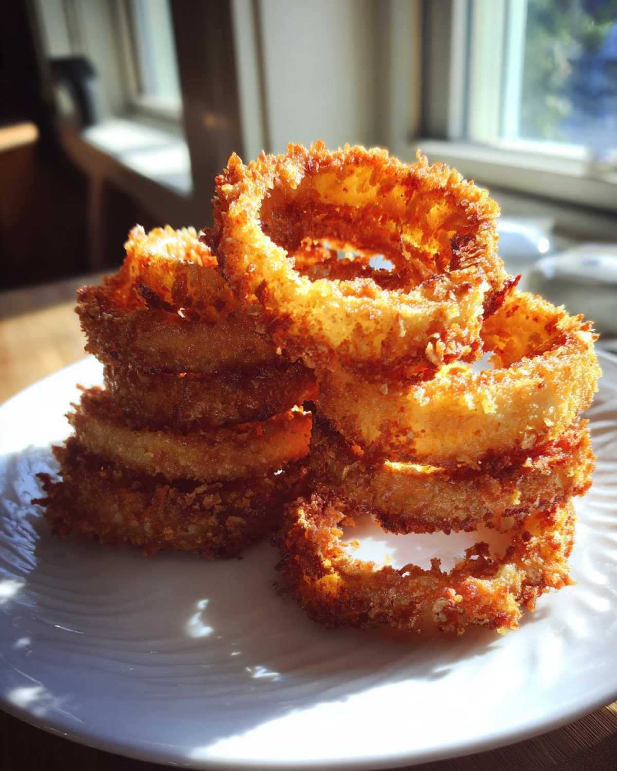 A stack of golden brown, crispy Air Fryer Onion Rings piled high on a white plate.