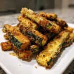 A close-up pile of crispy, golden Air Fryer Zucchini Fries with Parmesan on a white plate.