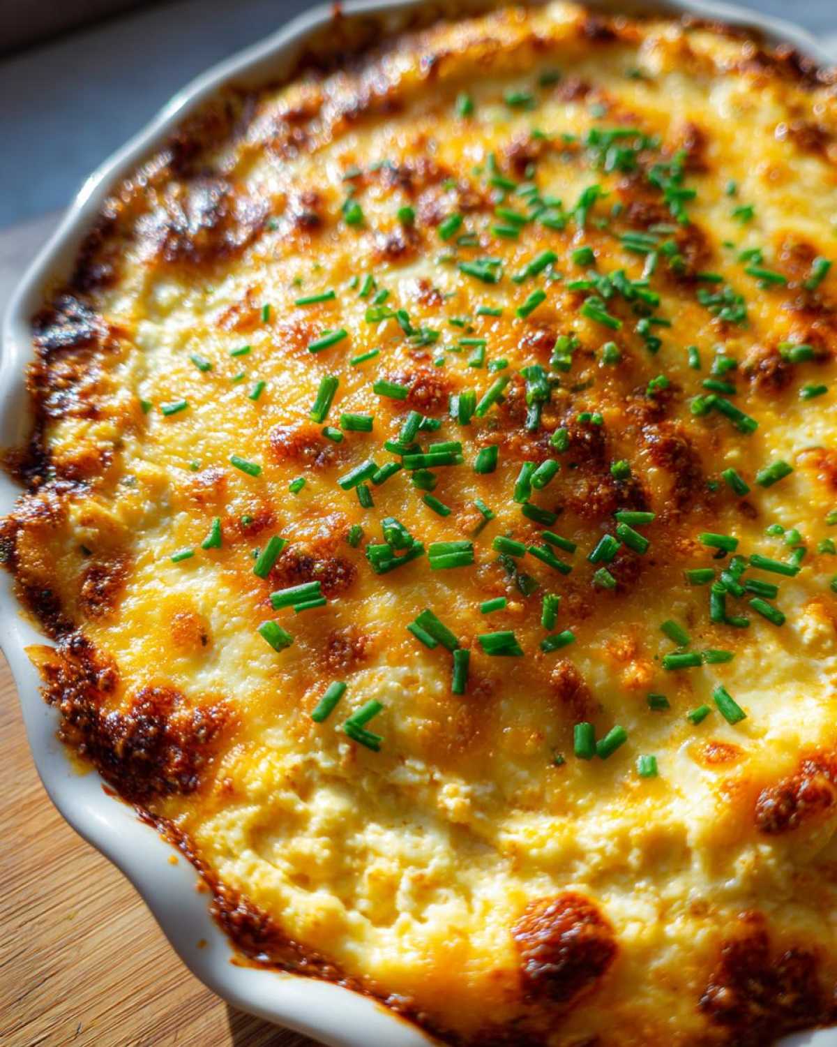 Close-up of hot Baked Buffalo Chicken Dip with a bubbly, browned cheese top garnished with fresh green chives.
