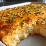 A scoop has been taken out of the Baked Buffalo Chicken Dip, revealing the creamy interior and golden-brown, cheesy top garnished with chives.