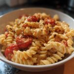 A close-up of creamy Baked Feta Pasta with Cherry Tomatoes mixed with fusilli pasta in a white bowl.