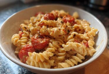 A close-up of creamy Baked Feta Pasta with Cherry Tomatoes mixed with fusilli pasta in a white bowl.