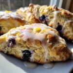 Close-up of freshly baked Blueberry Lemon Scones drizzled with white glaze and lemon zest.