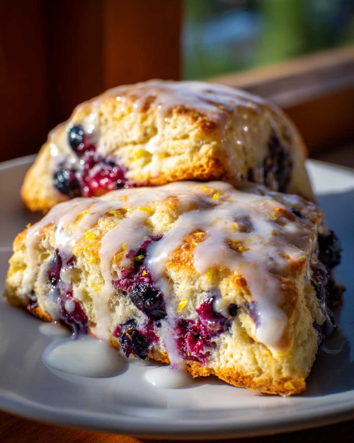 Two delicious Blueberry Lemon Scones stacked, drizzled with a thick lemon glaze and filled with burst blueberries.