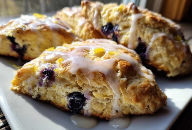 Close-up of freshly baked Blueberry Lemon Scones drizzled with white glaze and lemon zest.
