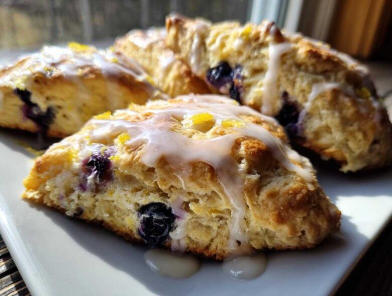 Close-up of freshly baked Blueberry Lemon Scones drizzled with white glaze and lemon zest.