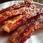 Close-up of crispy, caramelized Brown Sugar Glazed Bacon strips glistening on a white plate.