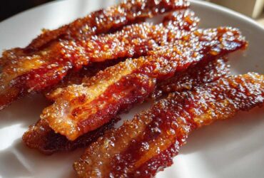 Close-up of crispy, caramelized Brown Sugar Glazed Bacon strips glistening on a white plate.