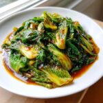 Close-up of vibrant green Cabbage Stir Fry with Garlic Ginger Sauce glistening in a rich brown sauce on a white plate.
