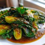 Close-up of vibrant green cabbage stir fry coated in rich garlic ginger sauce, served on a white plate.
