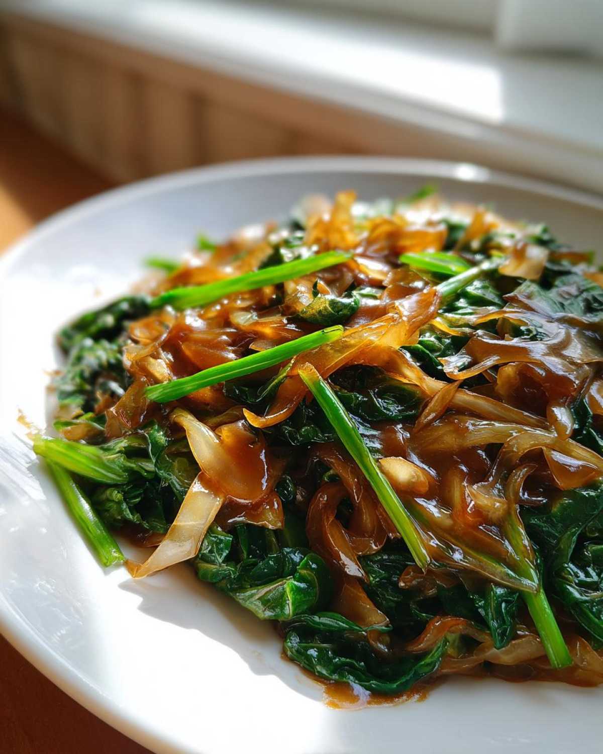 Close-up of Cabbage Stir Fry with Garlic Ginger Sauce, featuring wilted greens, caramelized onions, and bright green scallions.