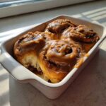 Close-up of warm Gluten-Free Cinnamon Rolls generously covered in thick caramel icing in a white baking dish.