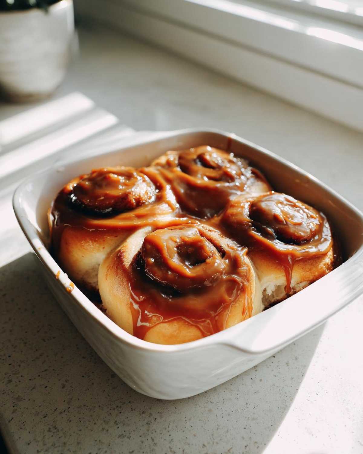 Four freshly baked Gluten-Free Cinnamon Rolls covered in thick caramel icing in a white square baking dish.
