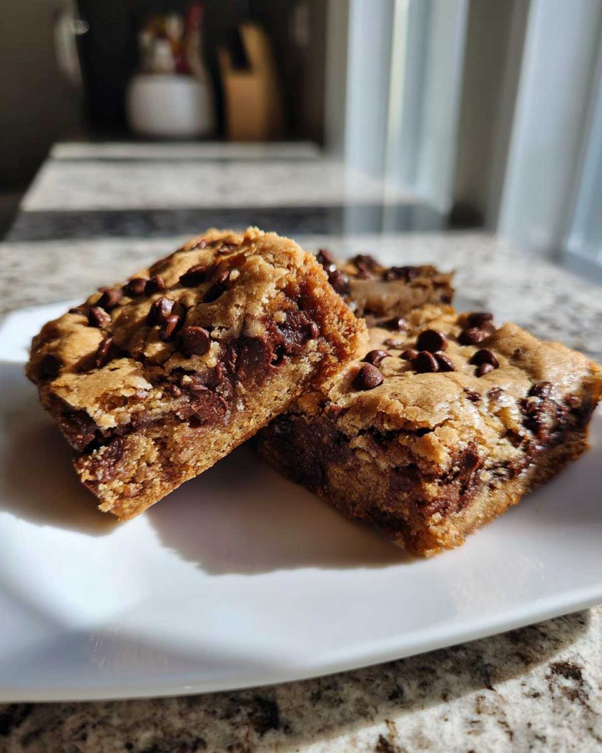 Two thick, golden Chewy Chocolate Chip Cookie Bars stacked slightly on a white plate, showing melted chocolate interior.