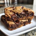 Two stacked Chewy Chocolate Chip Cookie Bars showing a gooey, melted chocolate center dripping down the side.
