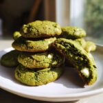 A stack of vibrant green, chewy matcha white chocolate cookies with one broken in half showing the soft interior.
