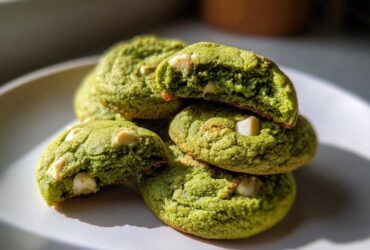 A stack of bright green, chewy matcha white chocolate cookies, one broken open to show the soft interior.